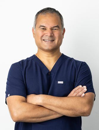 Smiling person in a navy shirt with arms crossed against a white background