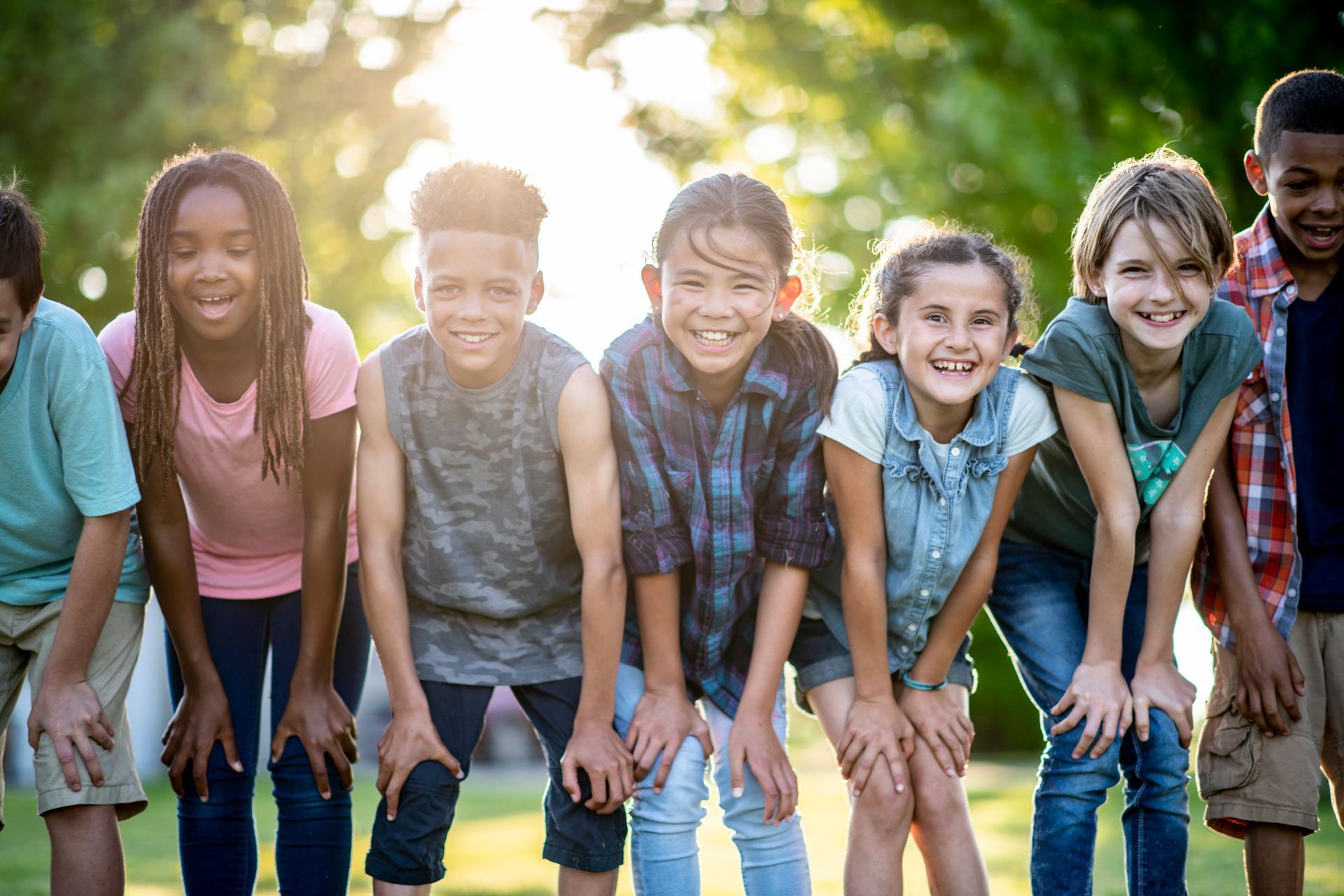 Group of smiling children leaning forward together in a sunny outdoor field