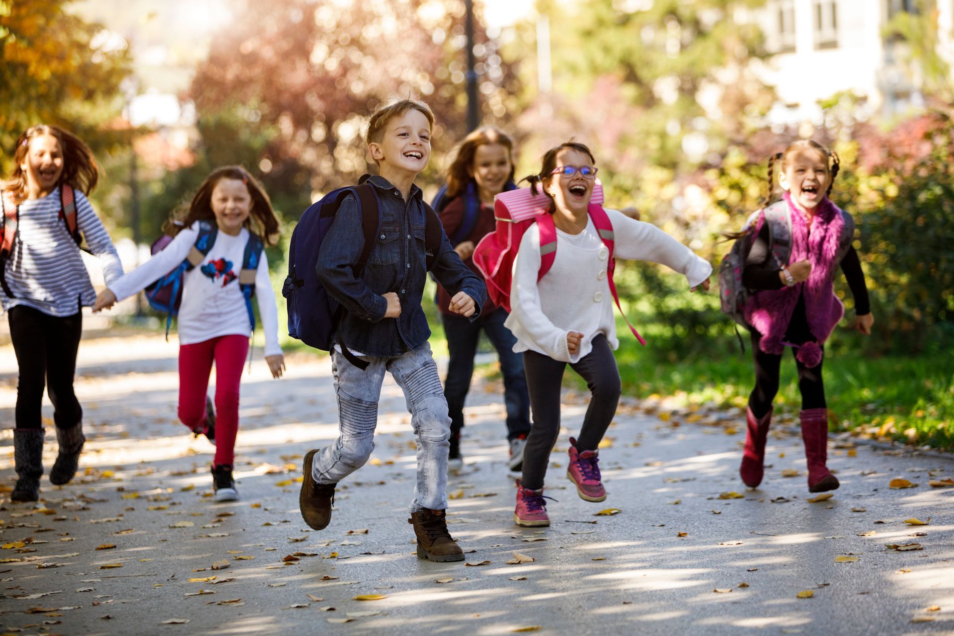 Children running and laughing on a tree-lined path in a sunny park