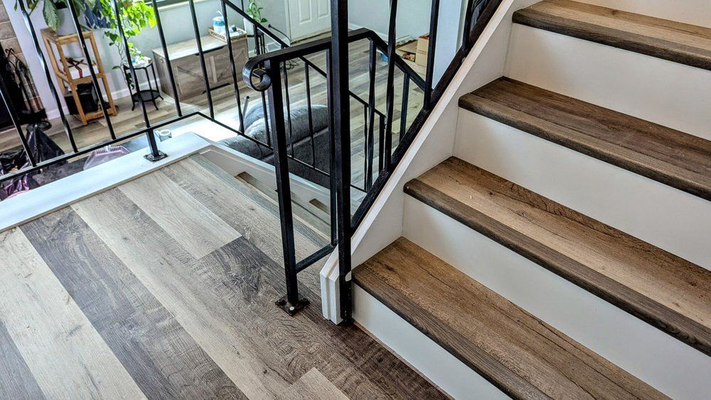 Staircase with wood-look steps and a black metal railing. Flooring is also wood-look. Sunlight visible through a window.