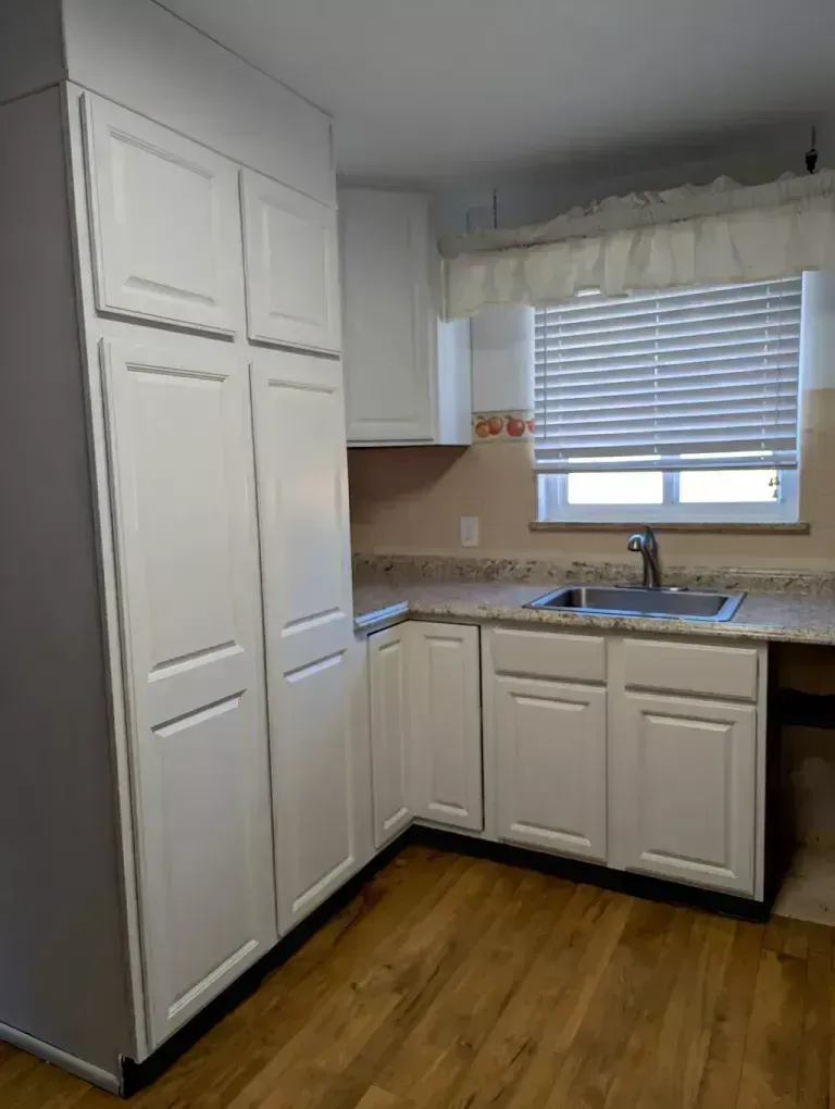 White kitchen cabinets with a sink and a window with blinds.