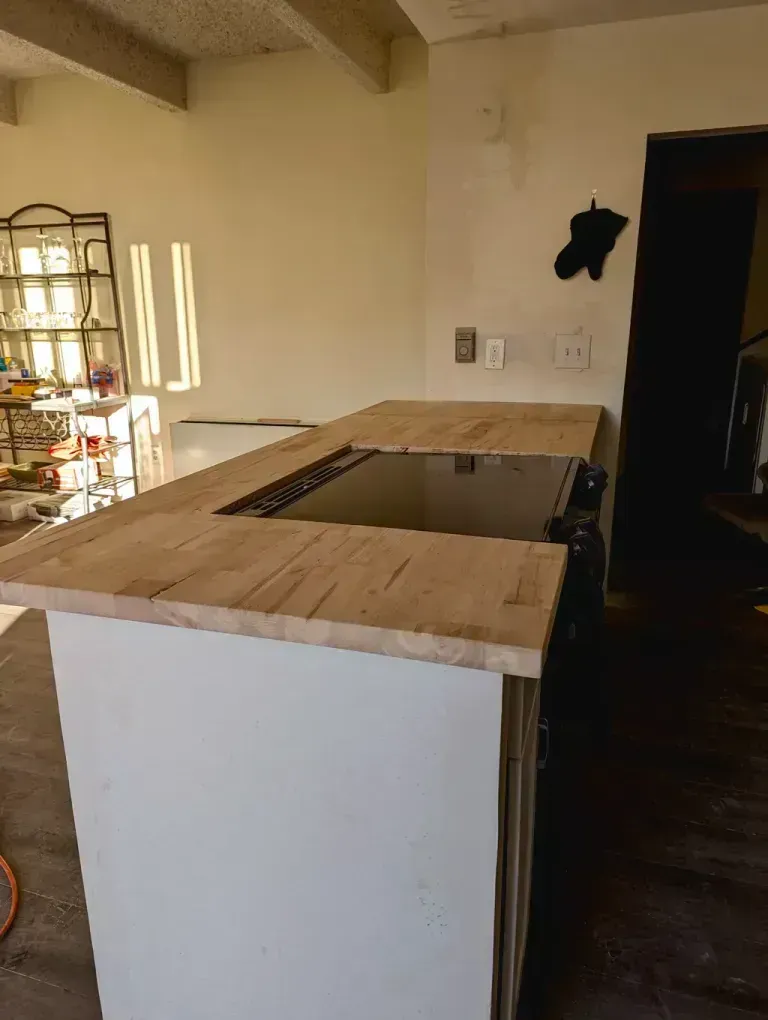 Kitchen island with a light wood countertop, white cabinets, and a cutout for a cooktop.