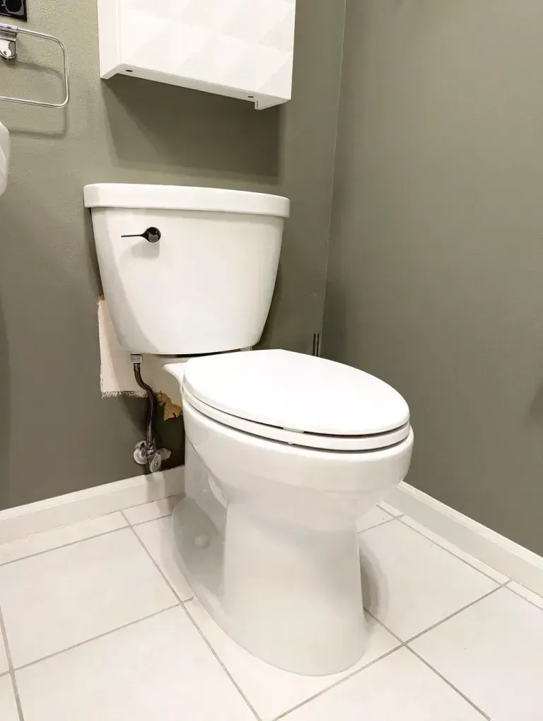 White toilet in a bathroom with white tiled floor and gray walls.