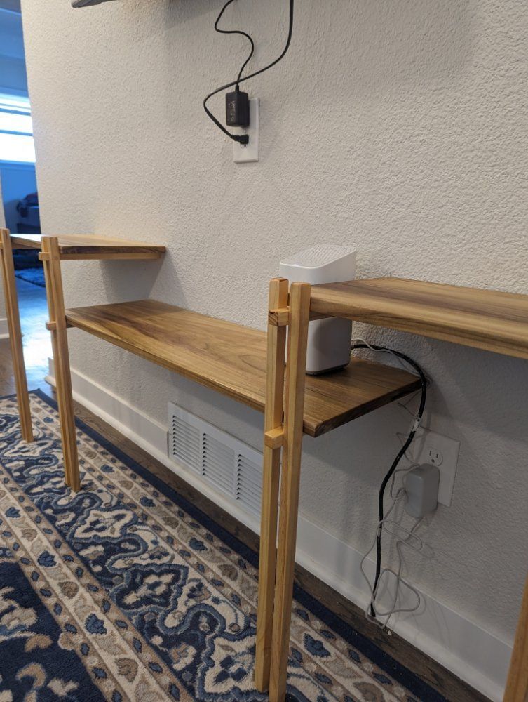 Wooden shelf with router on it, against a white wall with electrical outlets.