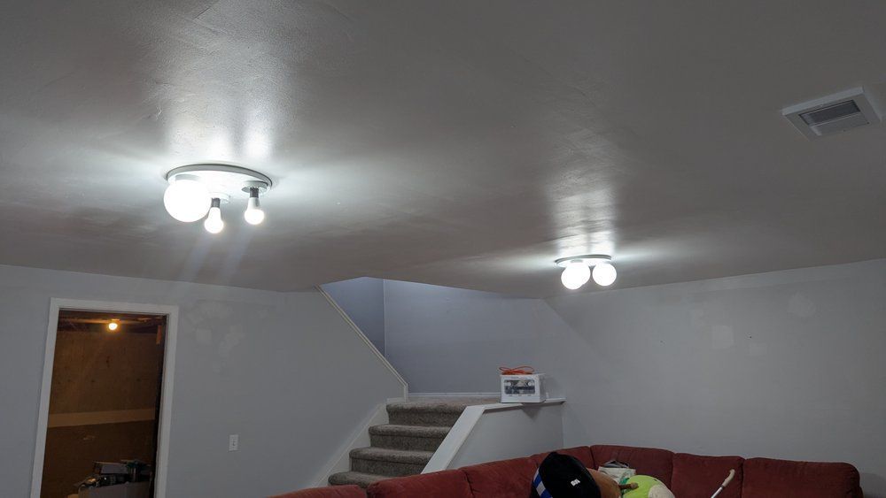 A basement interior with a staircase, couch, and ceiling lights, painted light gray.