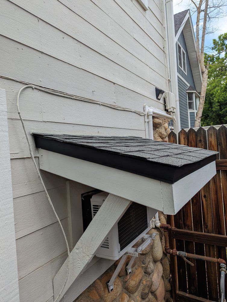 White and black awning covers an AC unit mounted on a stone wall, attached to a house with siding.