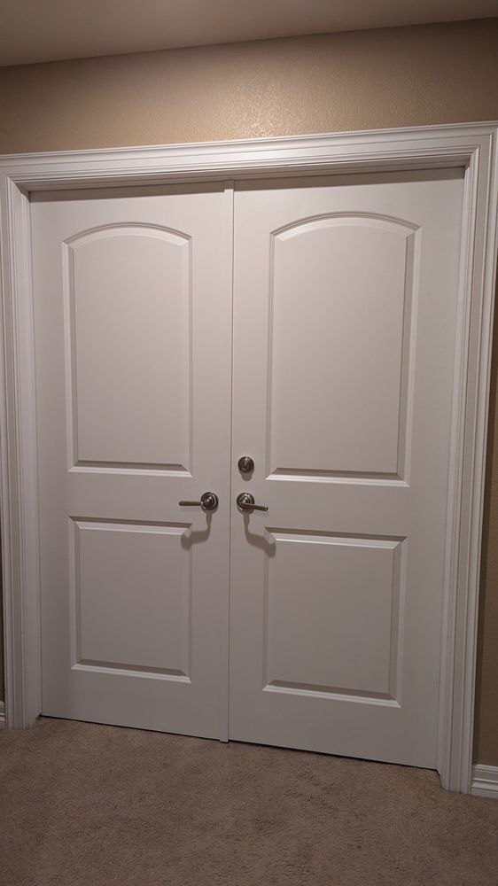 Double white doors with arched panels, silver door handles, and white trim.