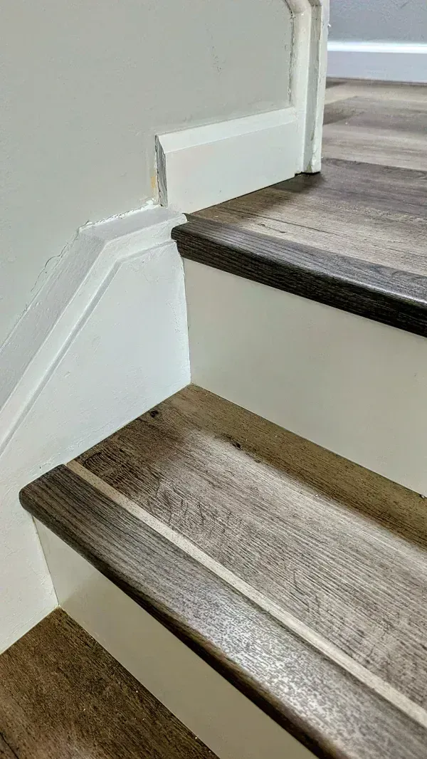 Wooden stairs with dark treads and white risers, leading up to a wall.