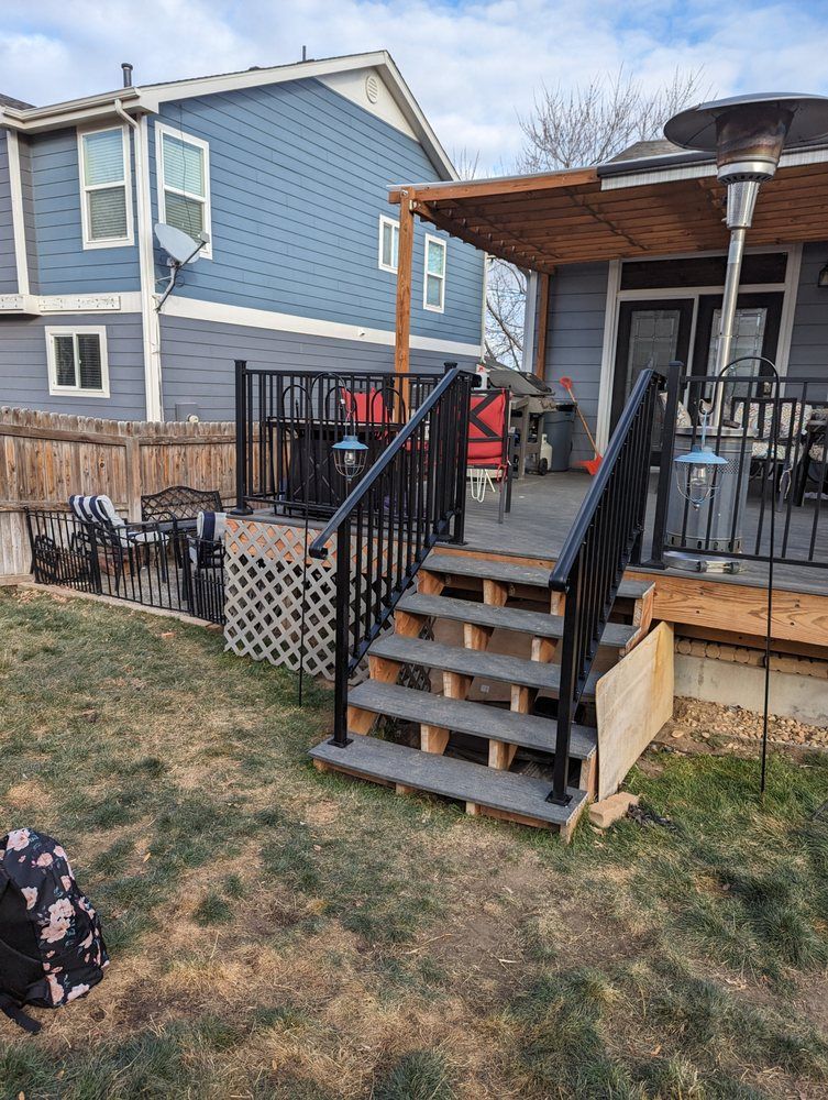 Wooden deck with black railings and steps leading to a backyard. A house is in the background.