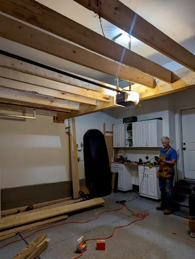 Garage interior with exposed beams, a man standing, looking at a phone.