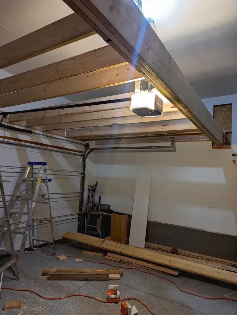 Garage ceiling being framed with wood beams and boards. Ladder and lumber on the floor.