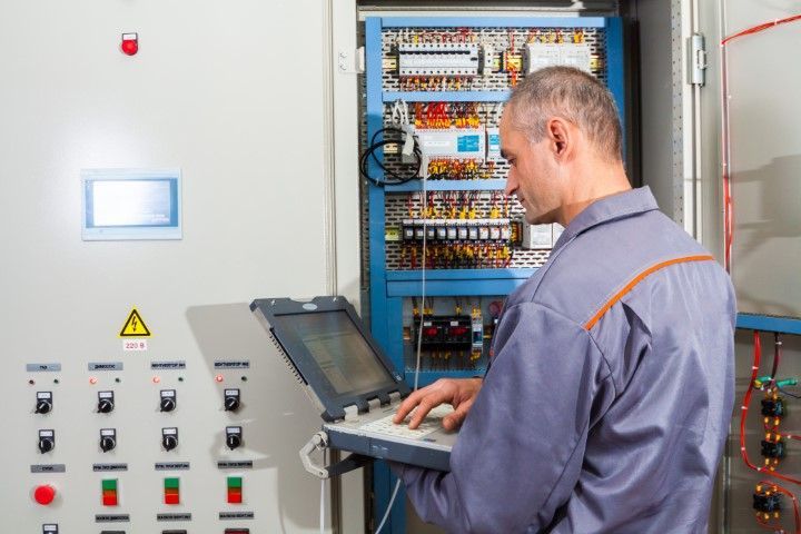 Man in work clothes uses a laptop to service electrical panel.