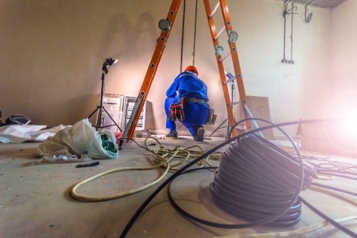 Electrician working on wiring inside a room, with a ladder and tools.
