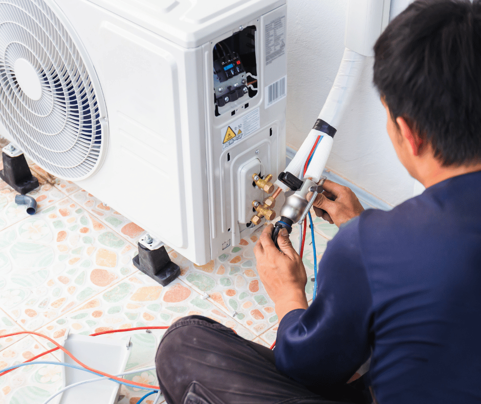 A man is sitting on the floor fixing an air conditioner.