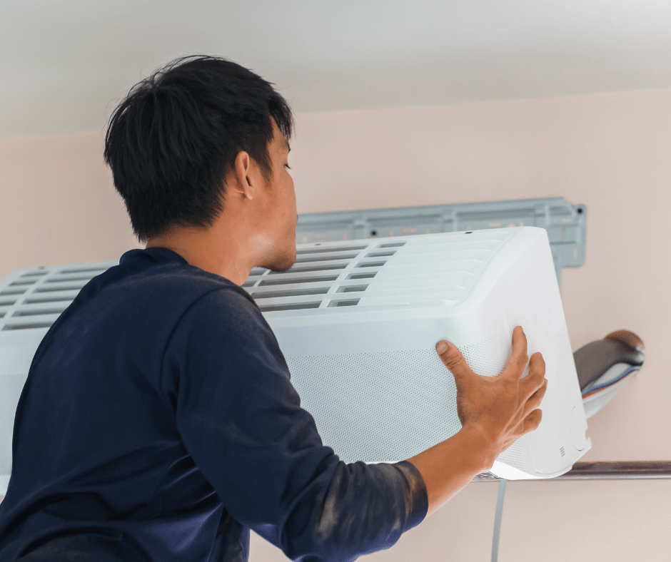 A man is installing an air conditioner on a wall.