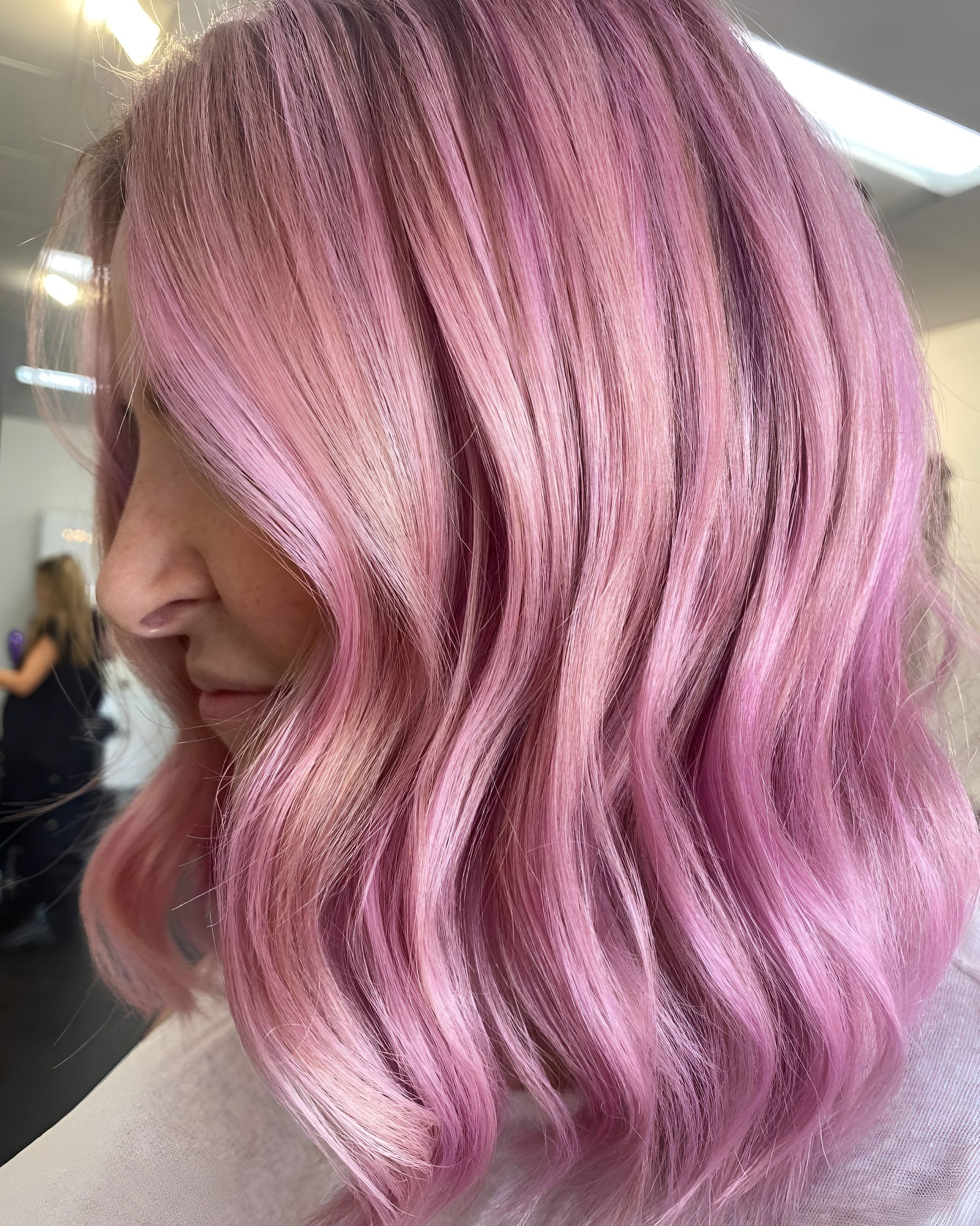 A profile view of a person with shoulder-length wavy hair coloured in shades of vibrant pink and deep magenta.