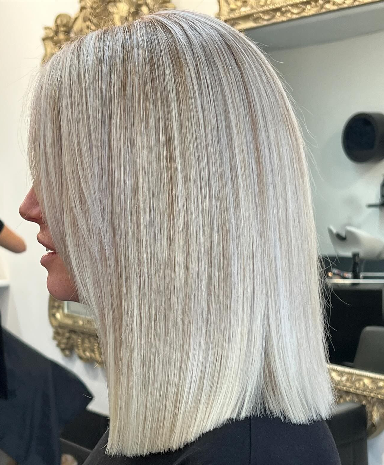 A person with shoulder-length, straight, platinum-blonde hair in a blunt-cut style, viewed from the side in a salon.