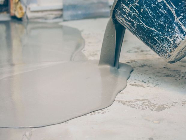 A person is pouring concrete into a puddle on the floor.
