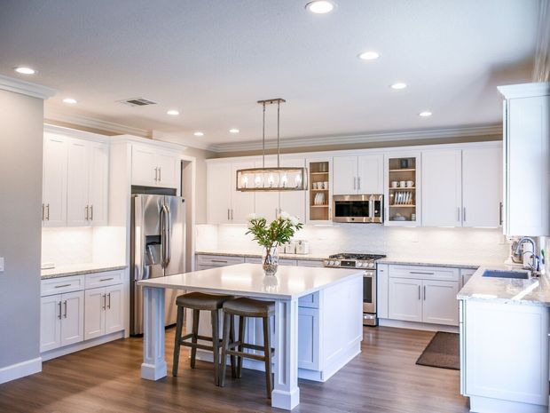 A kitchen with white cabinets , granite counter tops , stainless steel appliances and a large island.