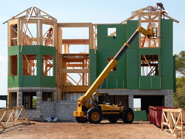 A large house is being built with a yellow forklift in front of it