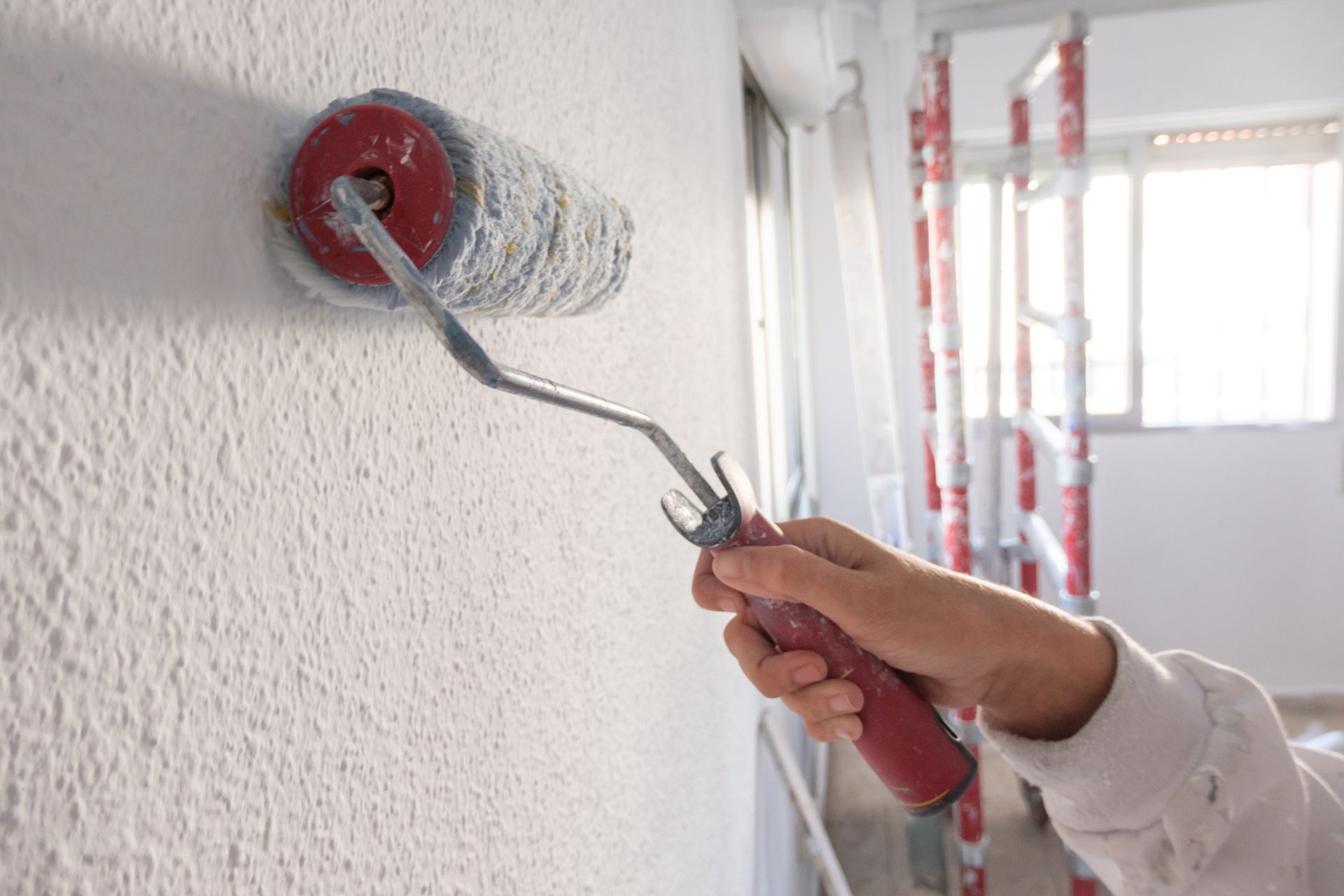 Peintre en casque bleu peignant un mur blanc avec un rouleau dans une pièce.