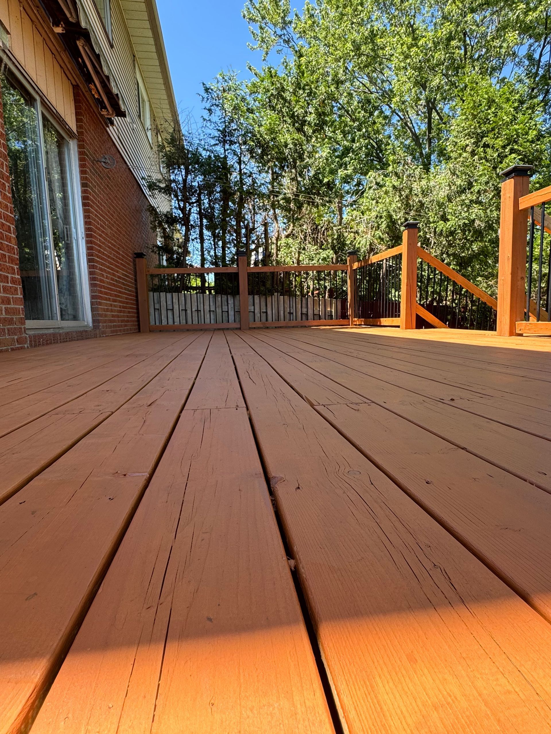 Terrasse en bois avec planches brunes, balustrade et extérieur du bâtiment en briques, journée ensoleillée.