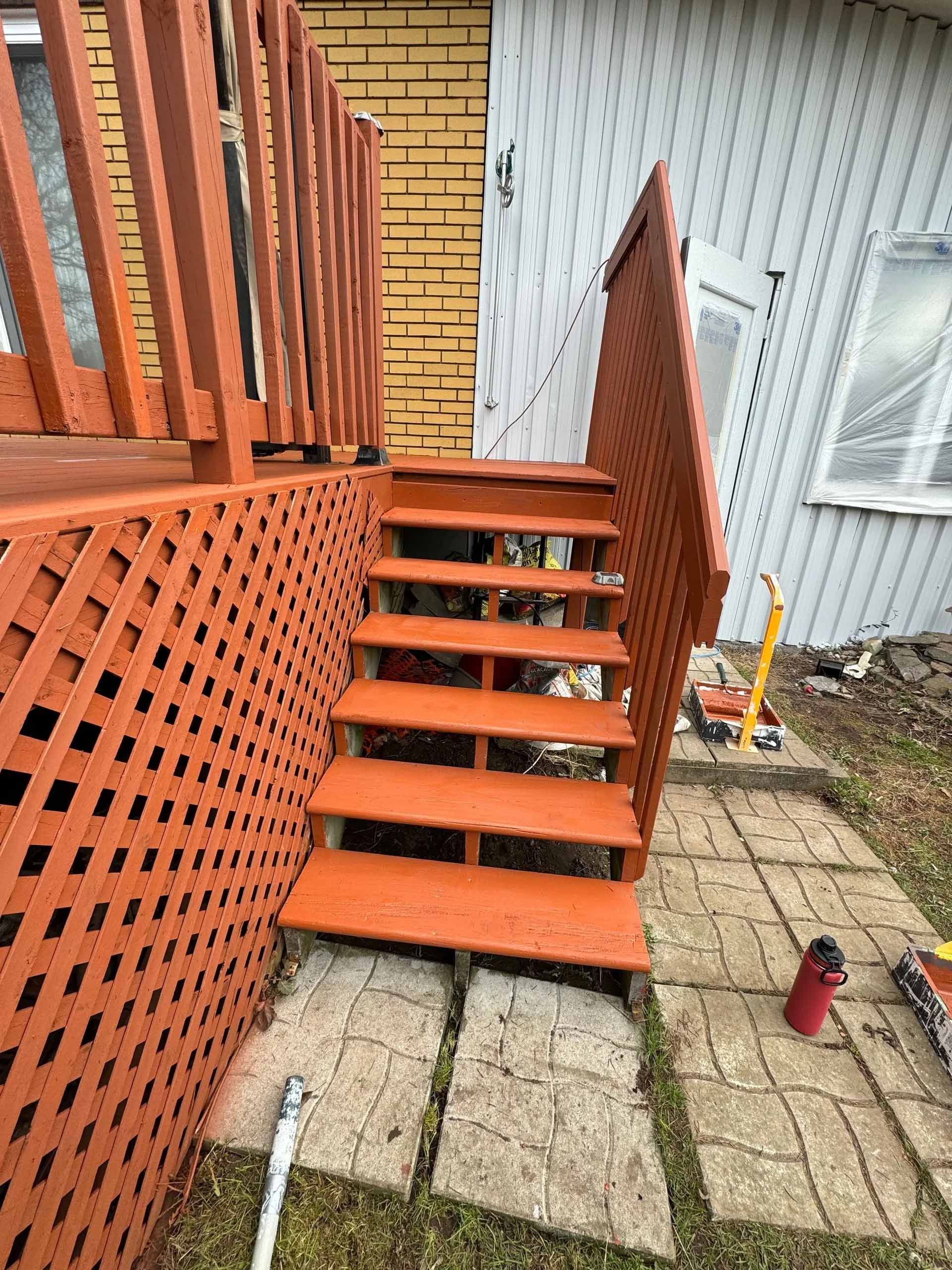 Escalier en bois peint en orange avec treillis, menant à une terrasse.