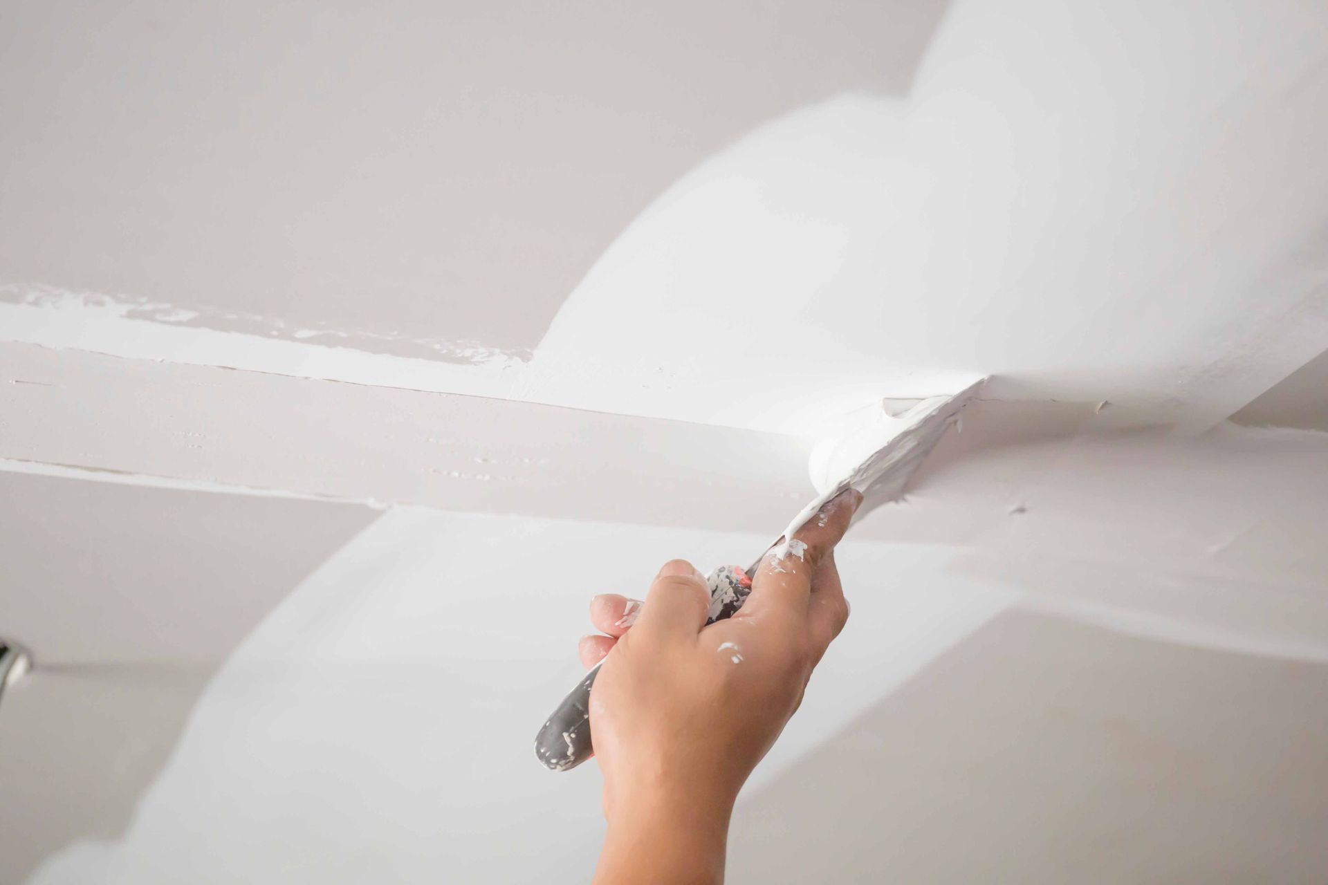 Un homme applique du plâtre sur un mur extérieur à l'aide d'une truelle.