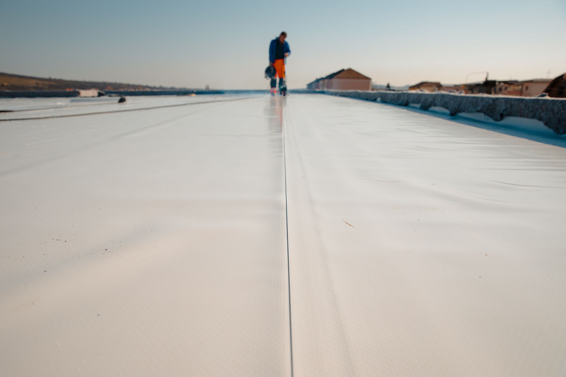 Worker applying white coating to a flat roof