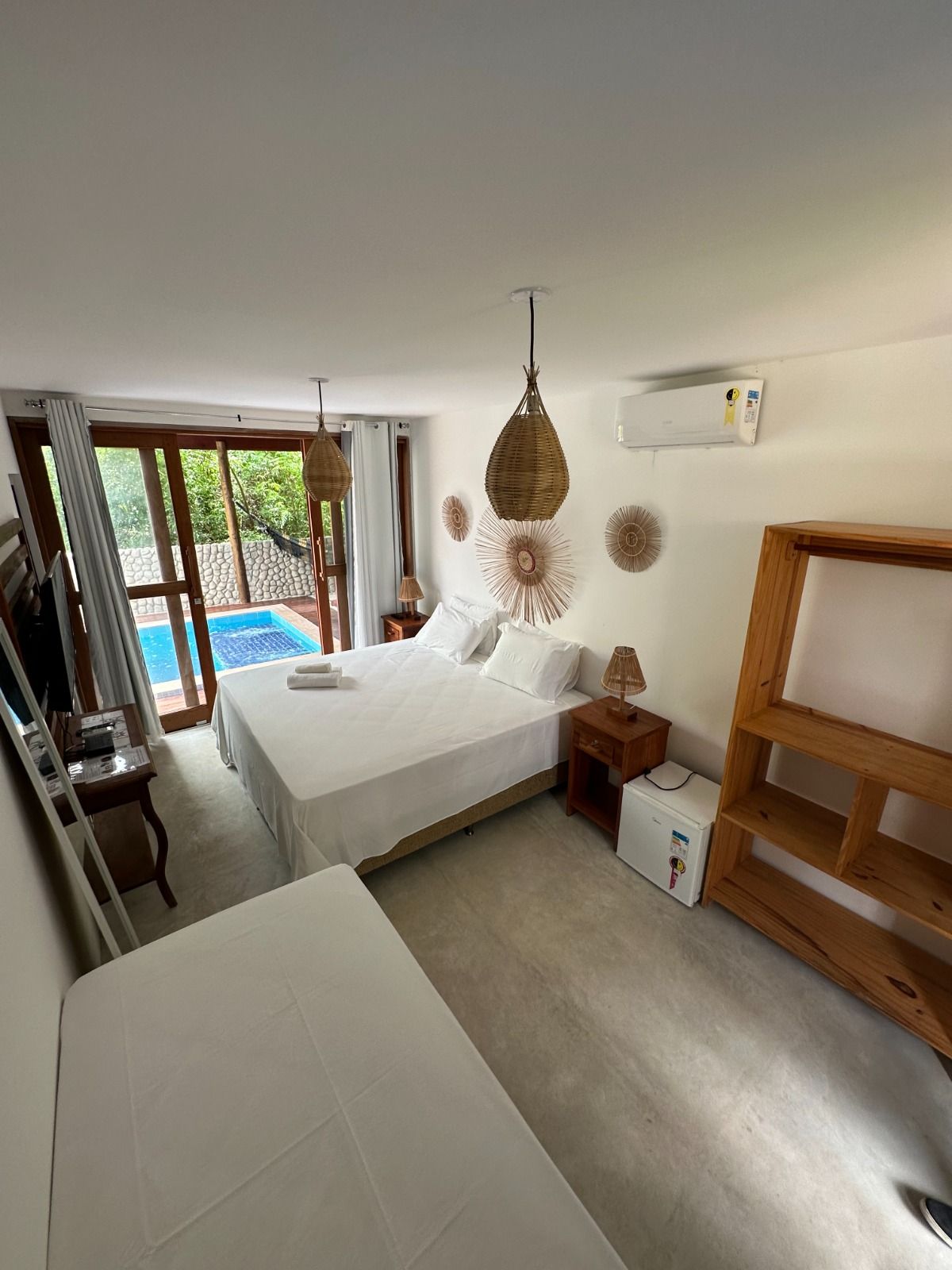 Um quarto de hotel minimalista e arejado, com cama de lençóis brancos, decoração natural e porta de vidro que dá acesso a uma piscina privativa.