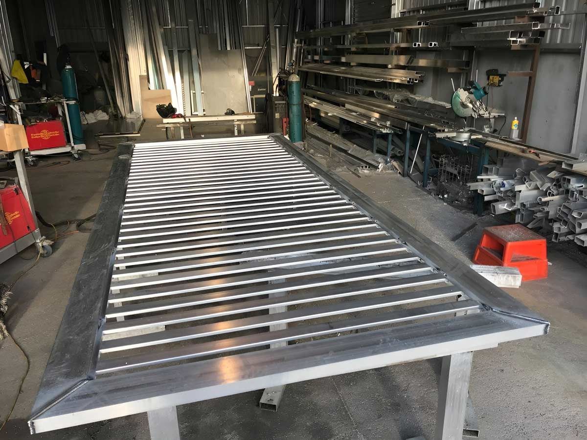 A large metal frame with evenly spaced slats on a worktable inside a workshop