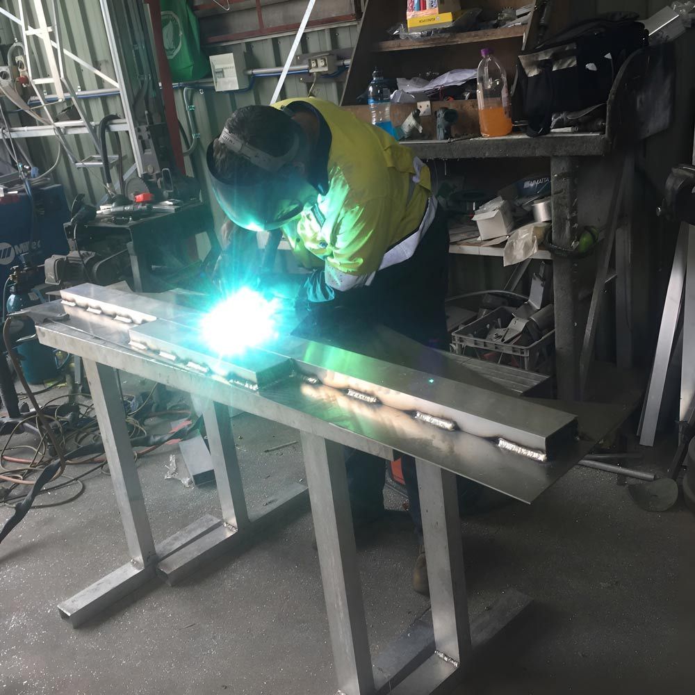 A Man Is Welding A Piece Of Metal In A Workshop — Brumb's Welding & Fabrication in Biggera Waters, QLD