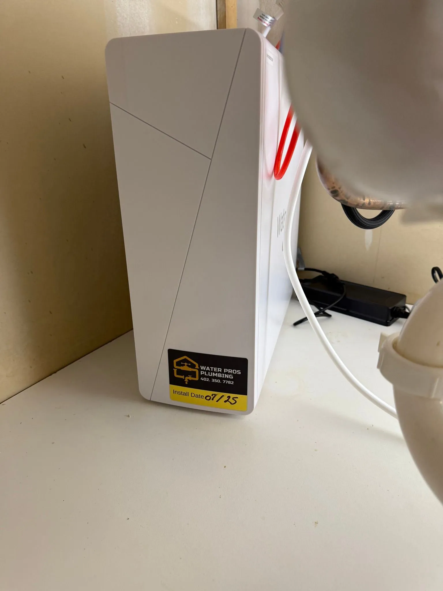 White rectangular device with a yellow sticker, near plumbing.