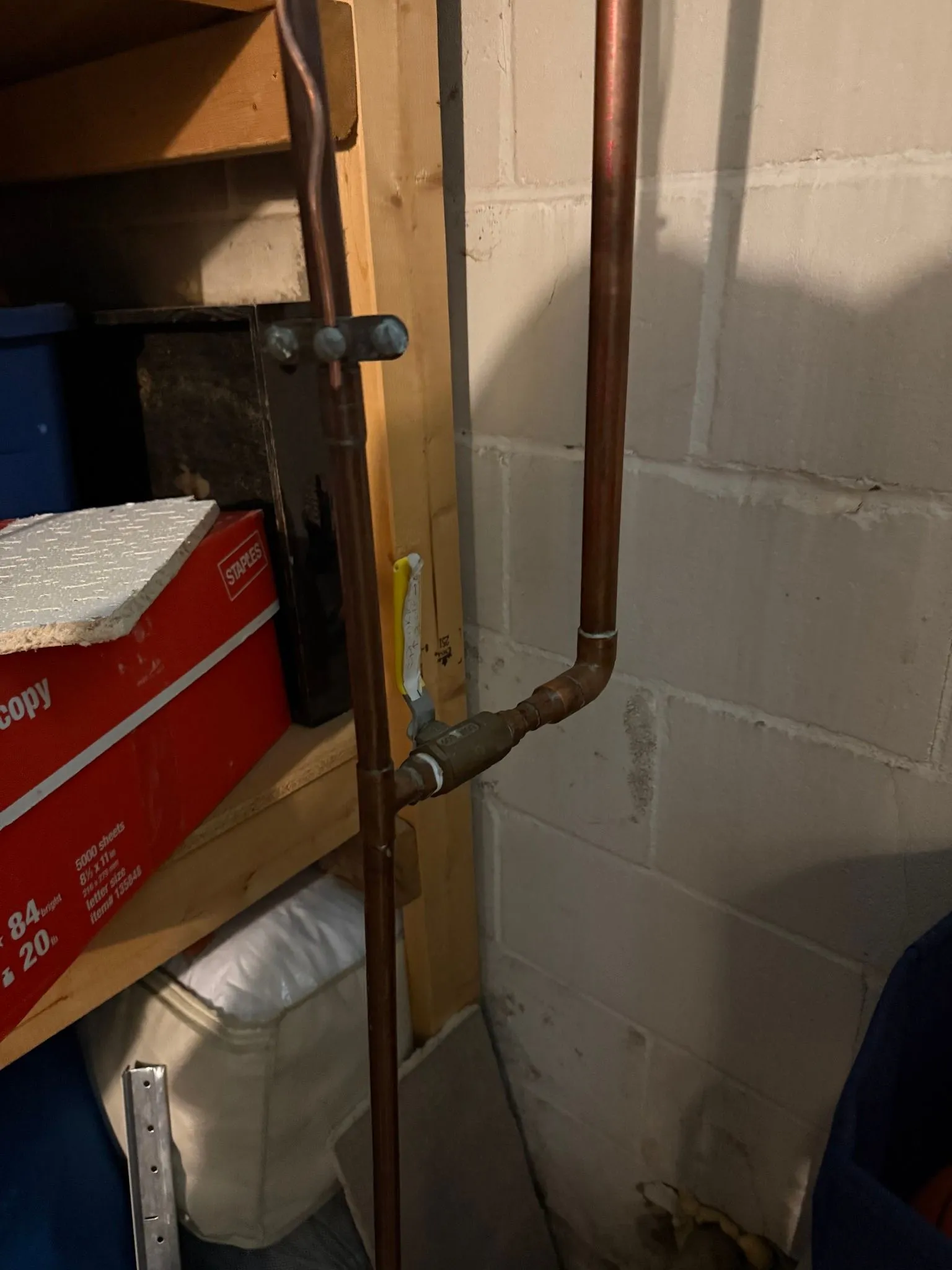 Copper pipes with a valve are installed on a concrete wall in a basement setting.
