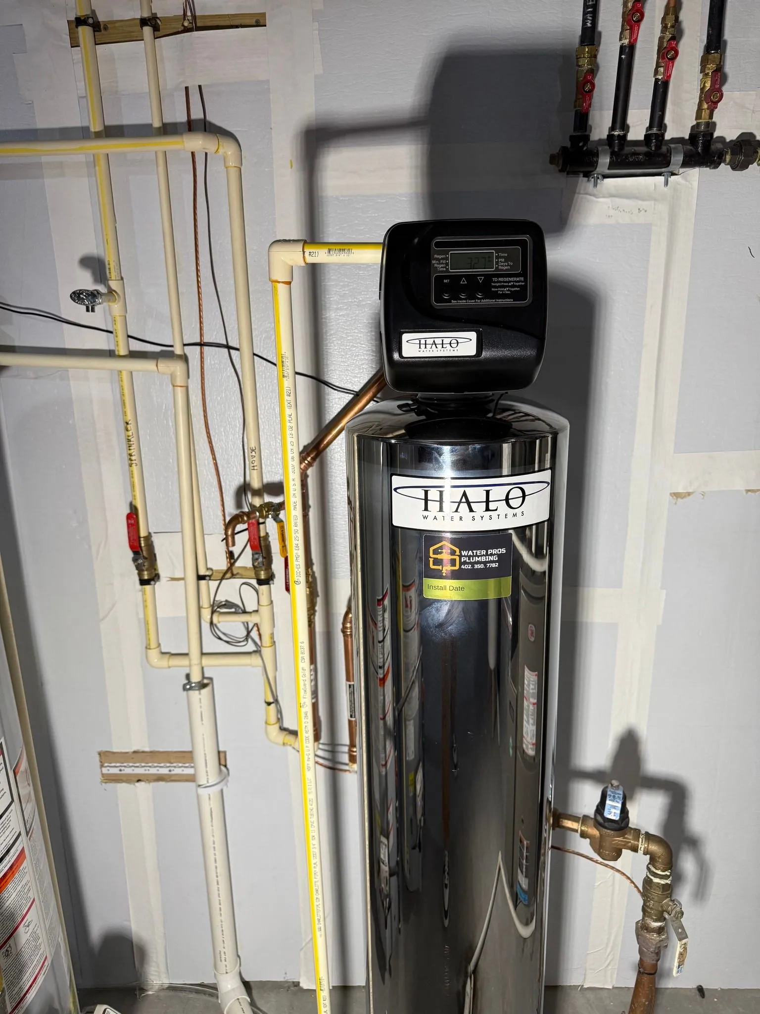 Water filtration system with black control panel and stainless steel tank, connected to plumbing.