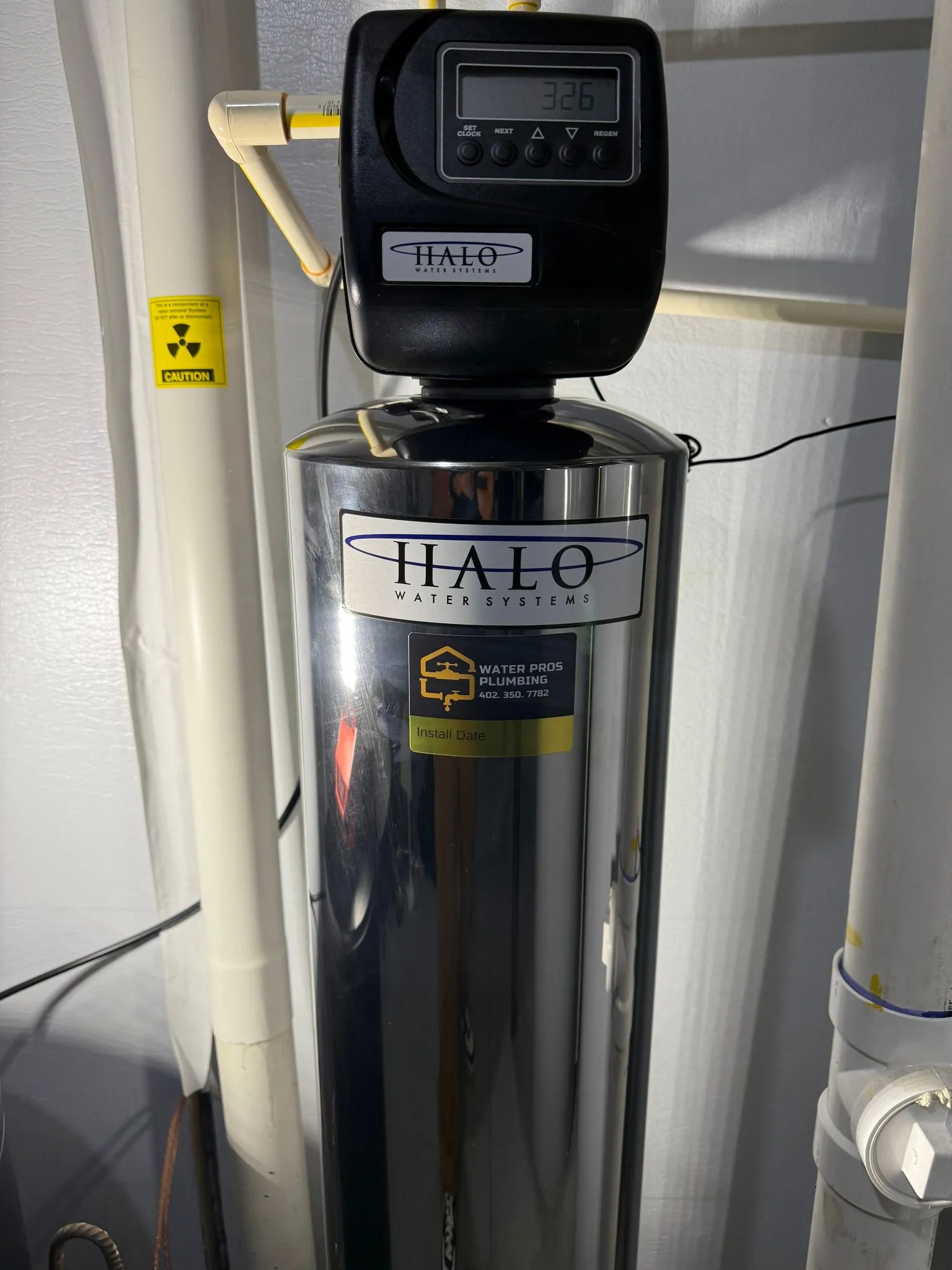 Halo water filtration system with digital display, installed near pipes and a tank.