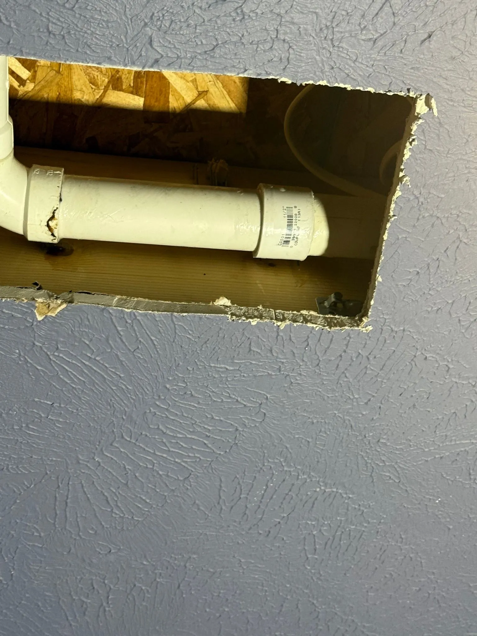 Hole in a blue wall revealing white PVC pipes within a wooden frame.