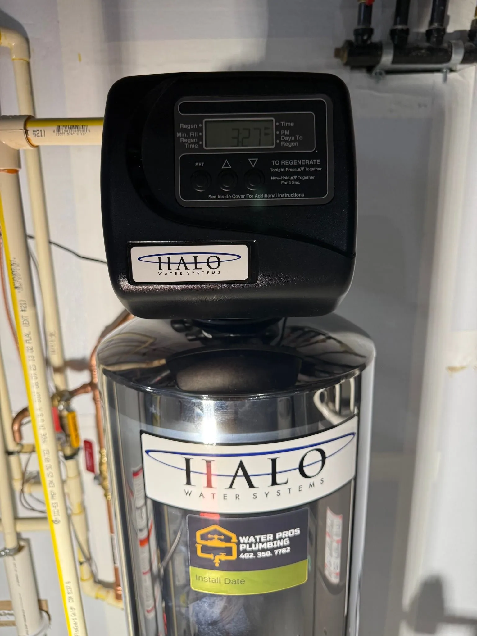 A Halo water filtration system. Black electronic display on top, stainless steel tank with Halo logo. Beige pipes.