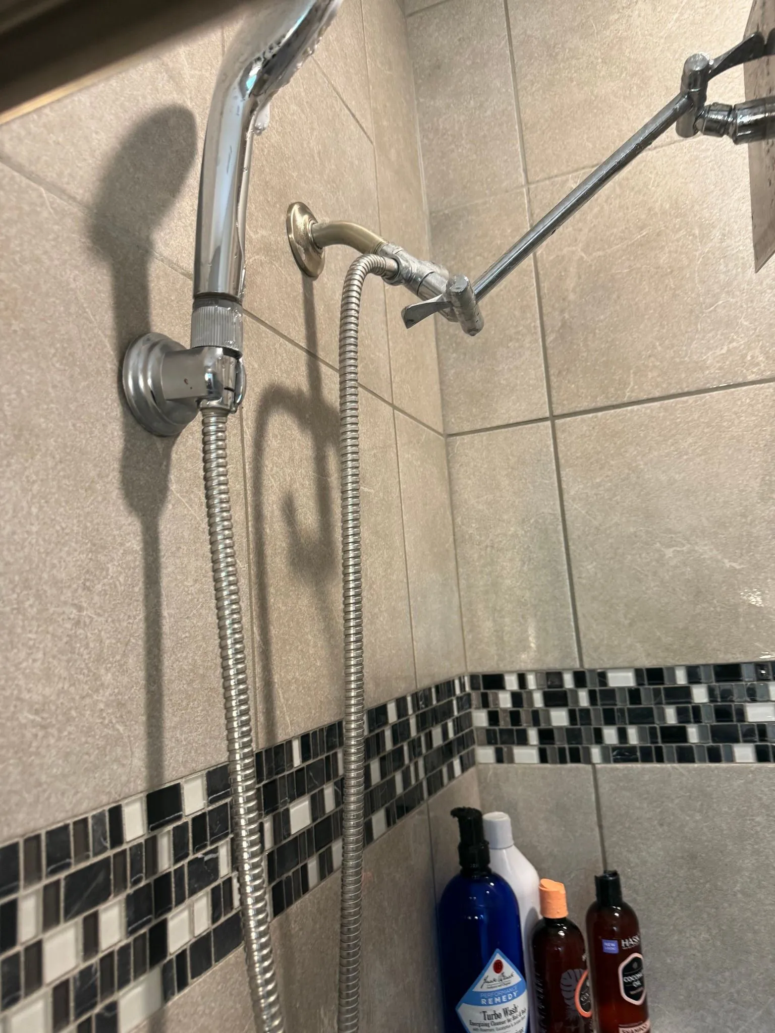 Shower with silver fixtures and a handheld shower head on tiled wall, with bottles below.