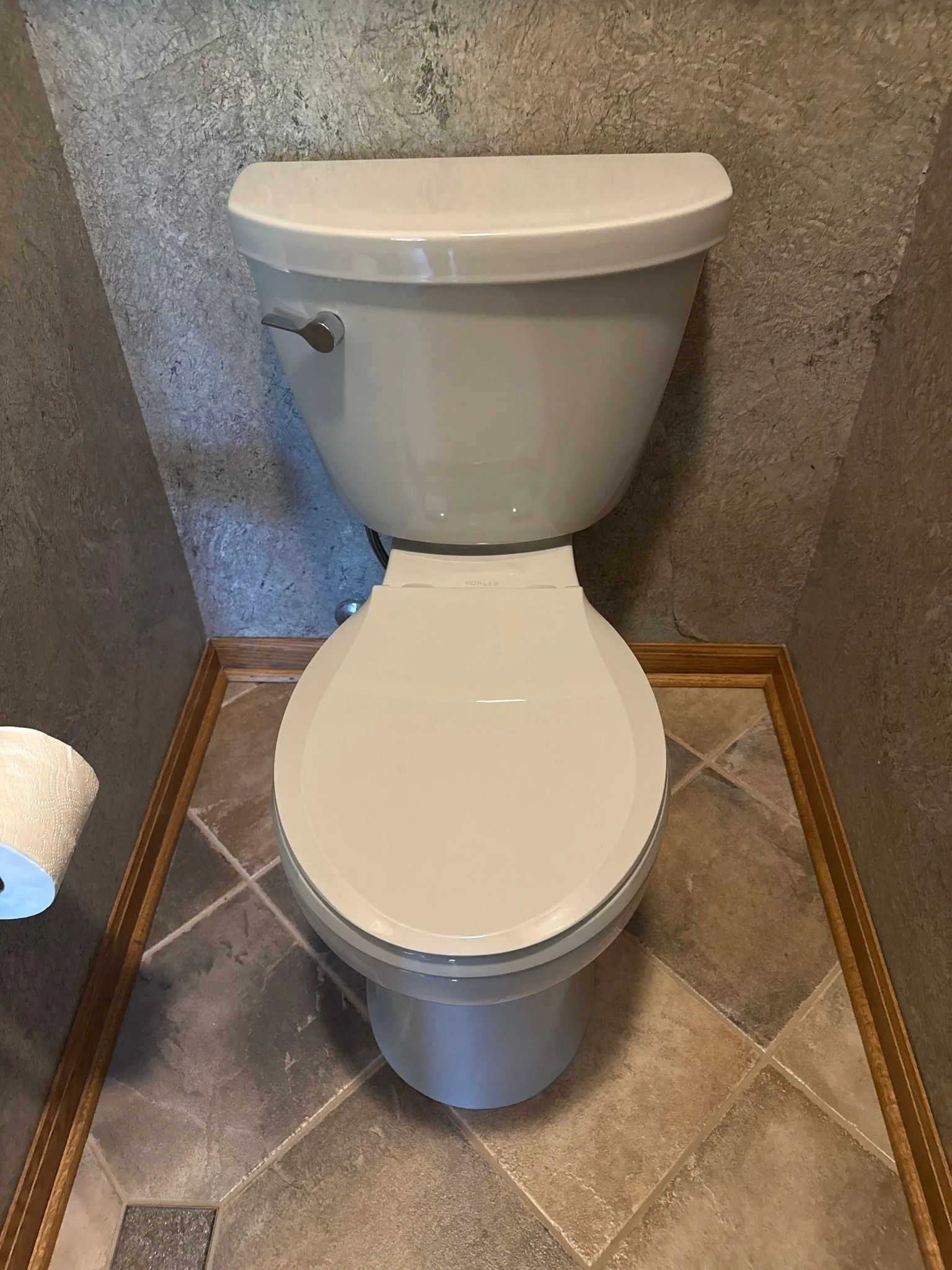 Toilet in a small bathroom nook, with gray walls, a closed white toilet seat, and tiled floor.