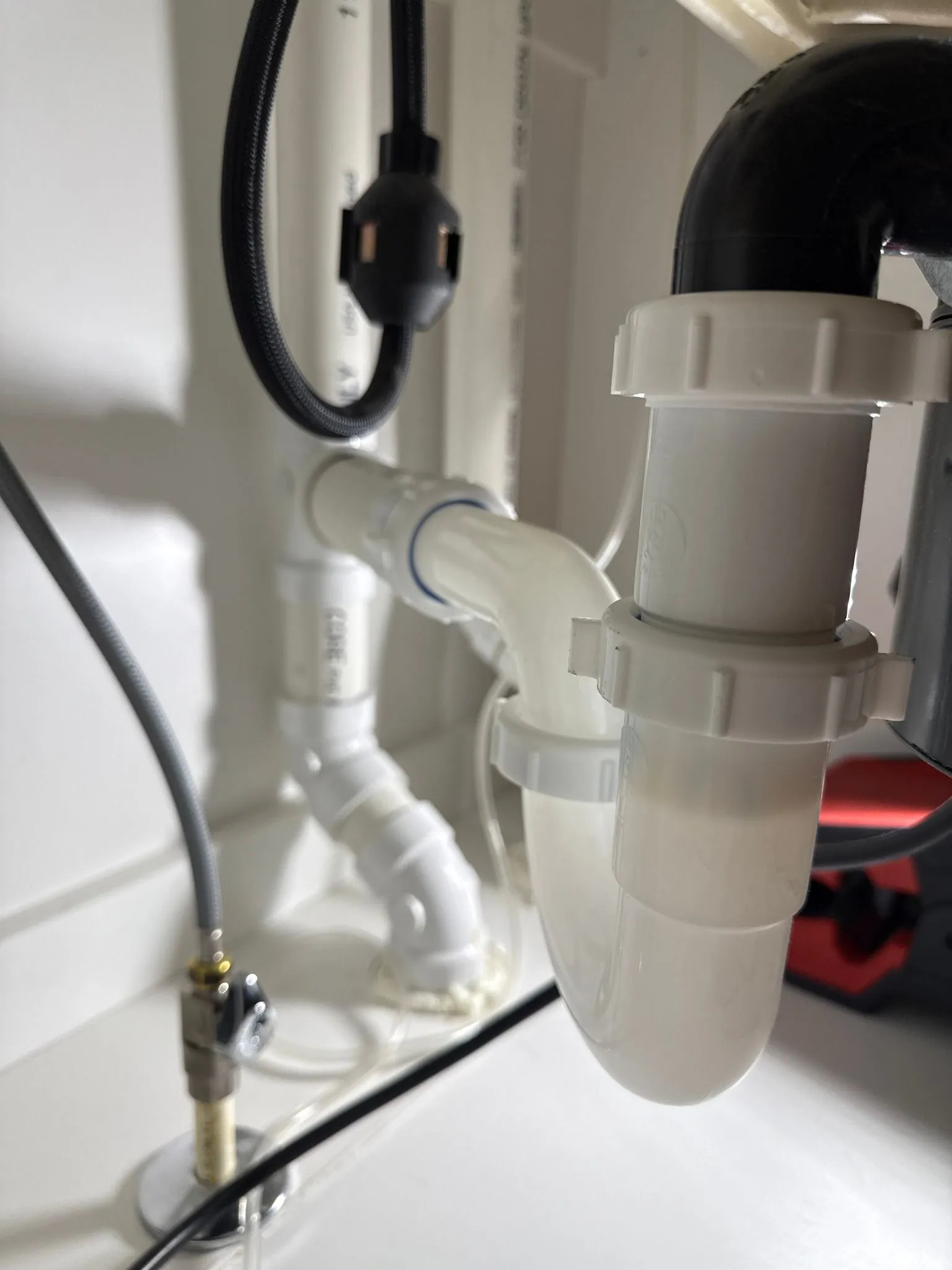 White sink plumbing under a cabinet: pipes, trap, drain.