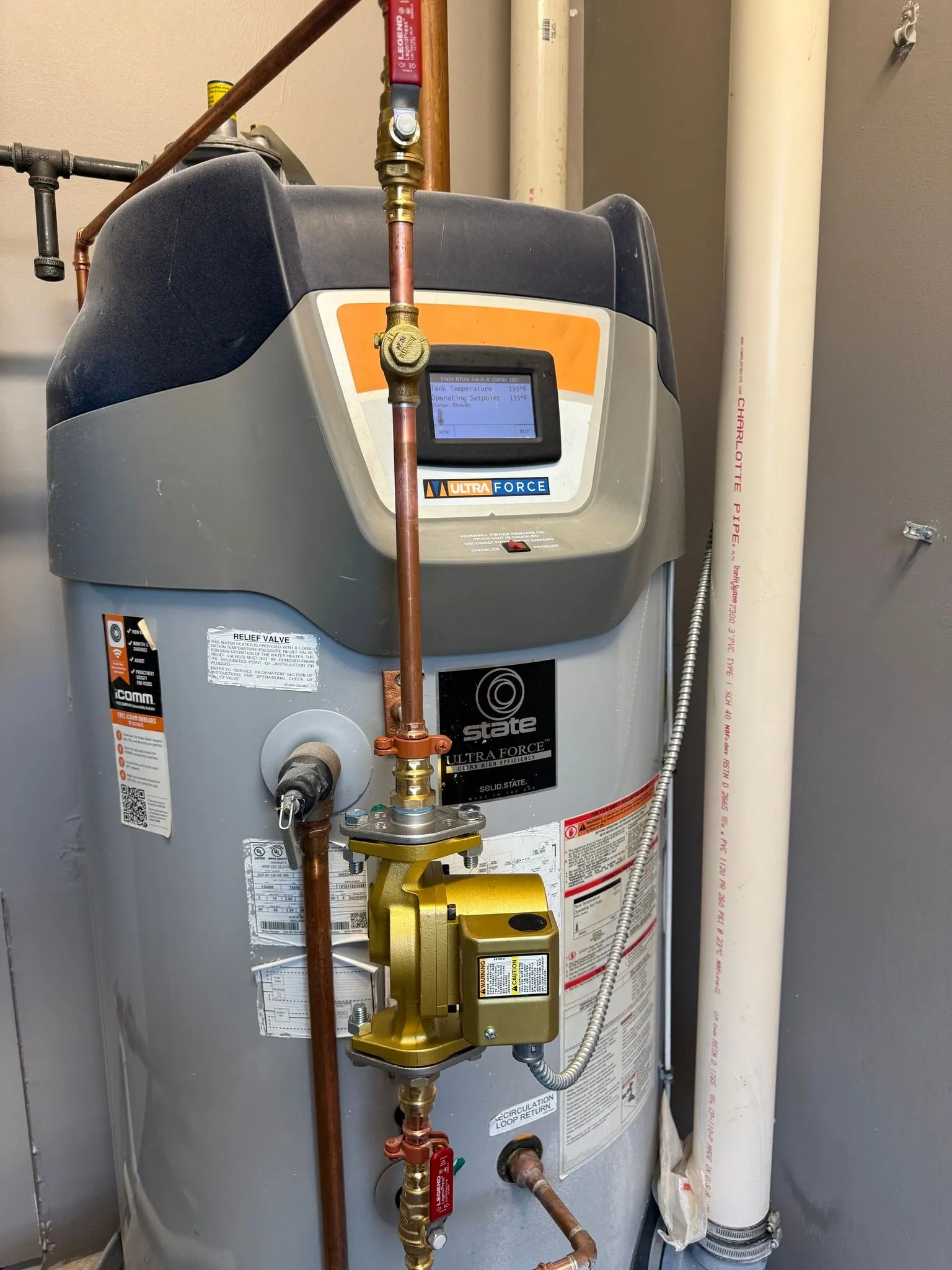A tall gray and blue water heater with copper pipes, valves, and a digital display in a utility room.