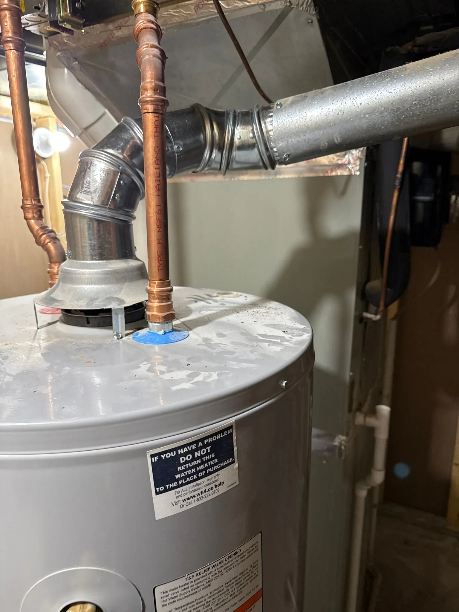 Water heater with copper pipes and metal flue in a basement.