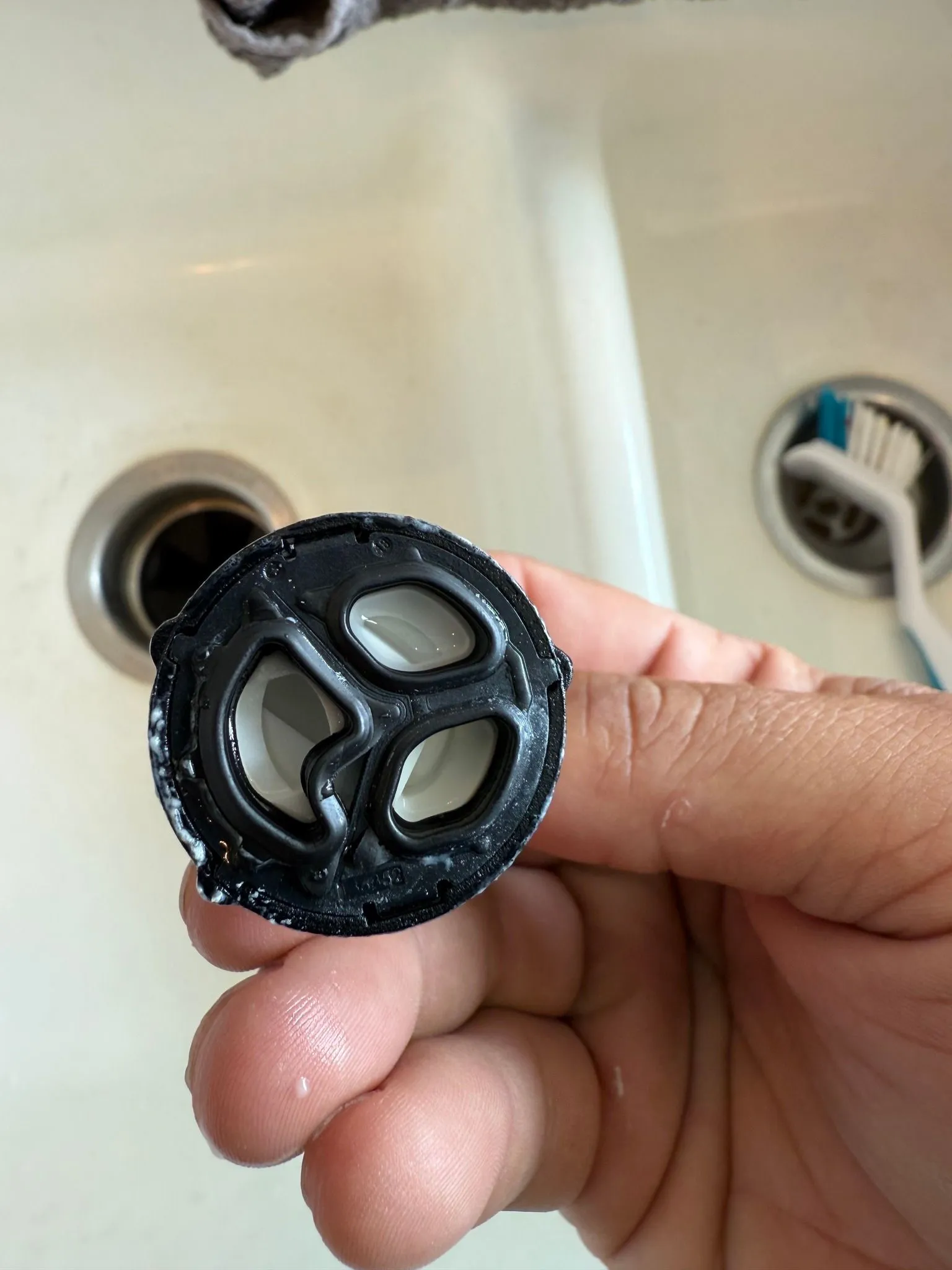 Hand holding a black faucet aerator with white interior, near a sink.
