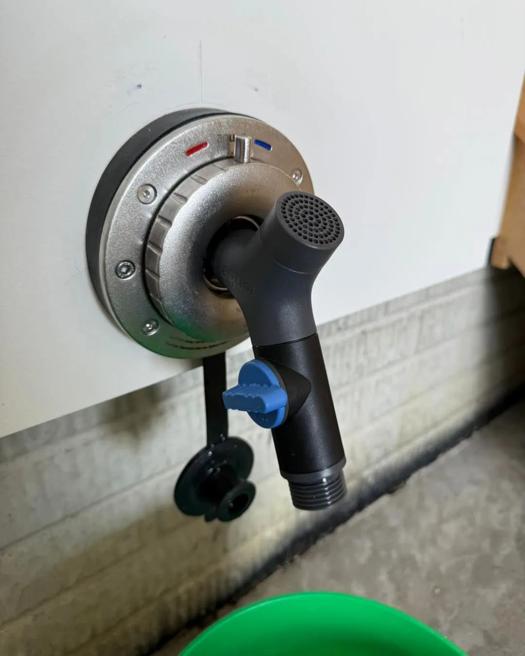 Wall-mounted faucet with black sprayer and blue valve. The faucet is silver with red/blue temperature indicators.