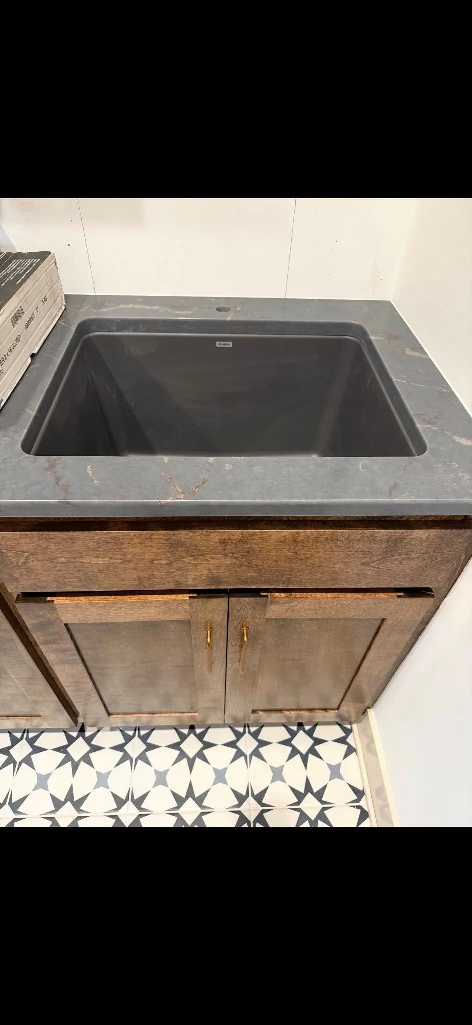 A dark gray sink is set into a wooden cabinet. The floor has a black and white patterned tile.