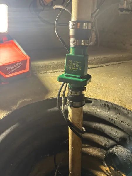 A sump pump system in a basement. Green check valve, black pipe, and a red work light.