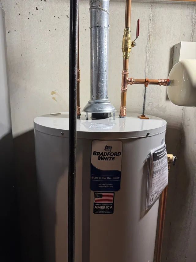 A tall, white Bradford White water heater in a basement. Copper pipes and vent pipe attached.