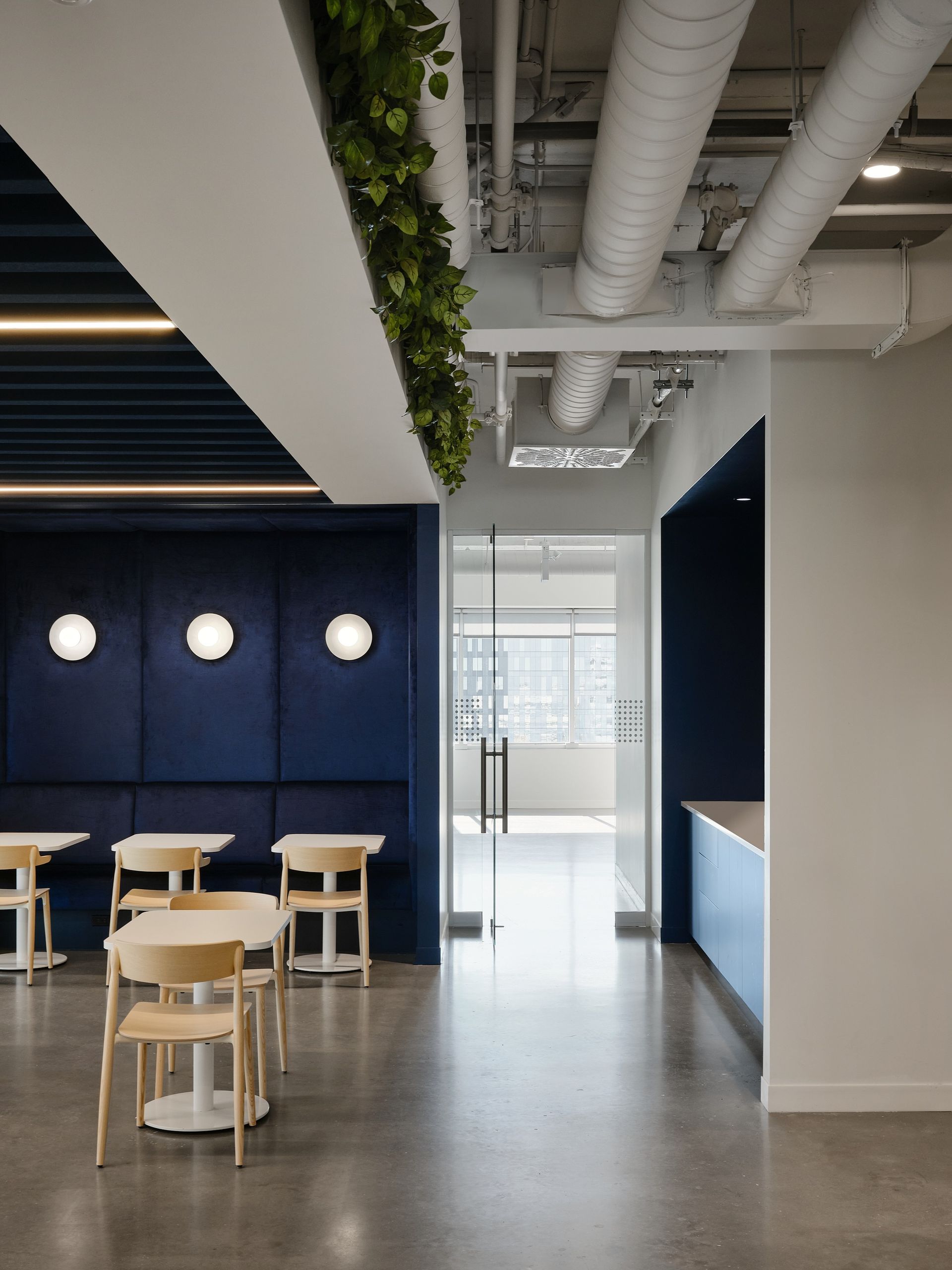 Salle de pause moderne avec mur capitonné bleu, tables et plantes.
