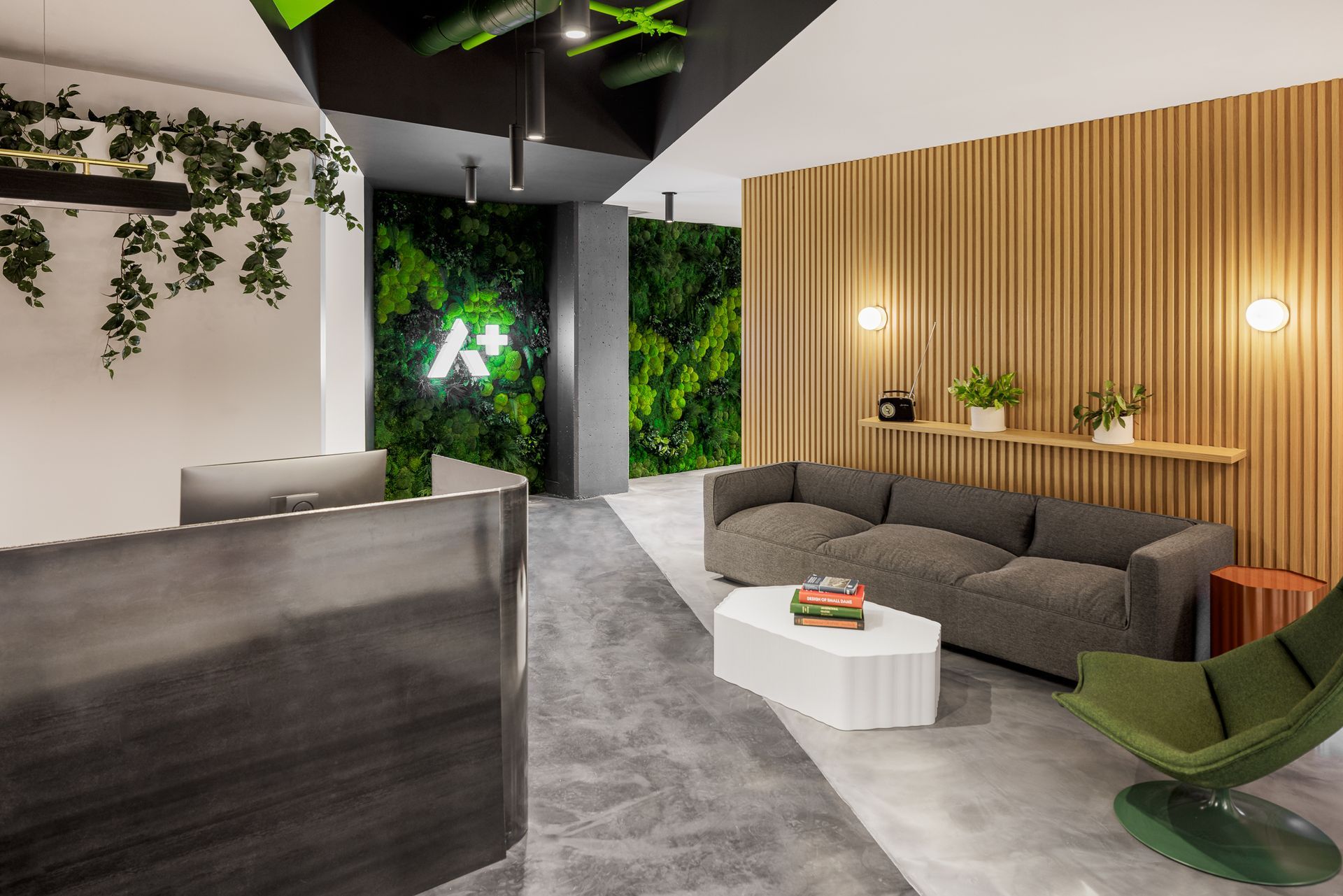 Espace d'accueil moderne avec un mur d'accent vert, des boiseries, un canapé gris et une table basse géométrique.